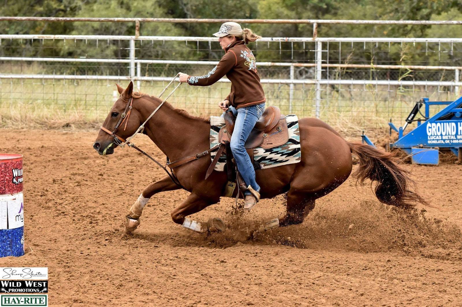 A rider on a chestnut horse rounding a barrel at speed, the horse low through the turn and dirt flying.